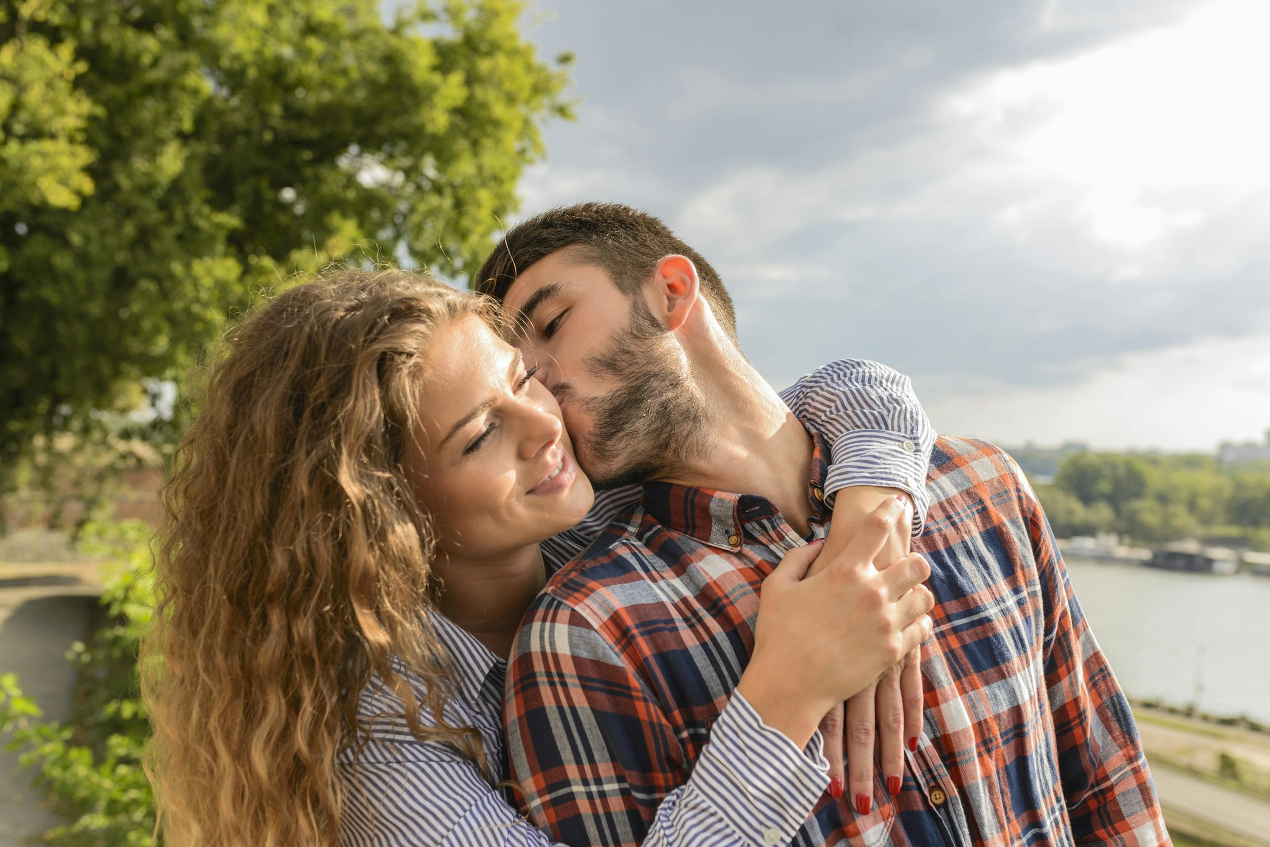 Happy couple sharing a loving embrace outdoors with a scenic background.